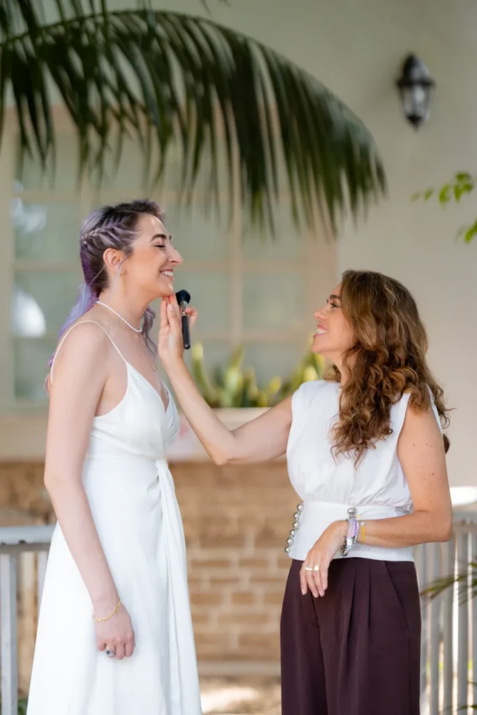 Professional makeup artist applying face highlighter to a bride's cheekbones for a natural glowing finish.